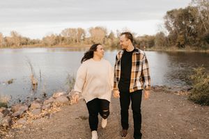 Couple walking hand in hand along a scenic riverside during fall engagement photos.