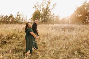 Couple laughs together in a sunlit golden field during an autumn engagement photo session at sunset.