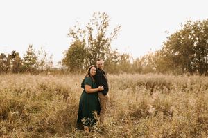 Woman in green dress embraced by partner in golden autumn field at sunset.