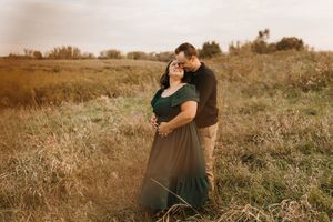 Romantic couple cuddling in tall grass field during warm golden hour engagement shoot.