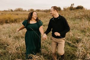 Happy couple holds hands and runs through a golden autumn field during a joyful engagement photo session.