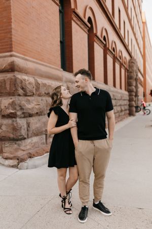 Couple laughing and walking together along a city sidewalk beside a classic red brick building.
