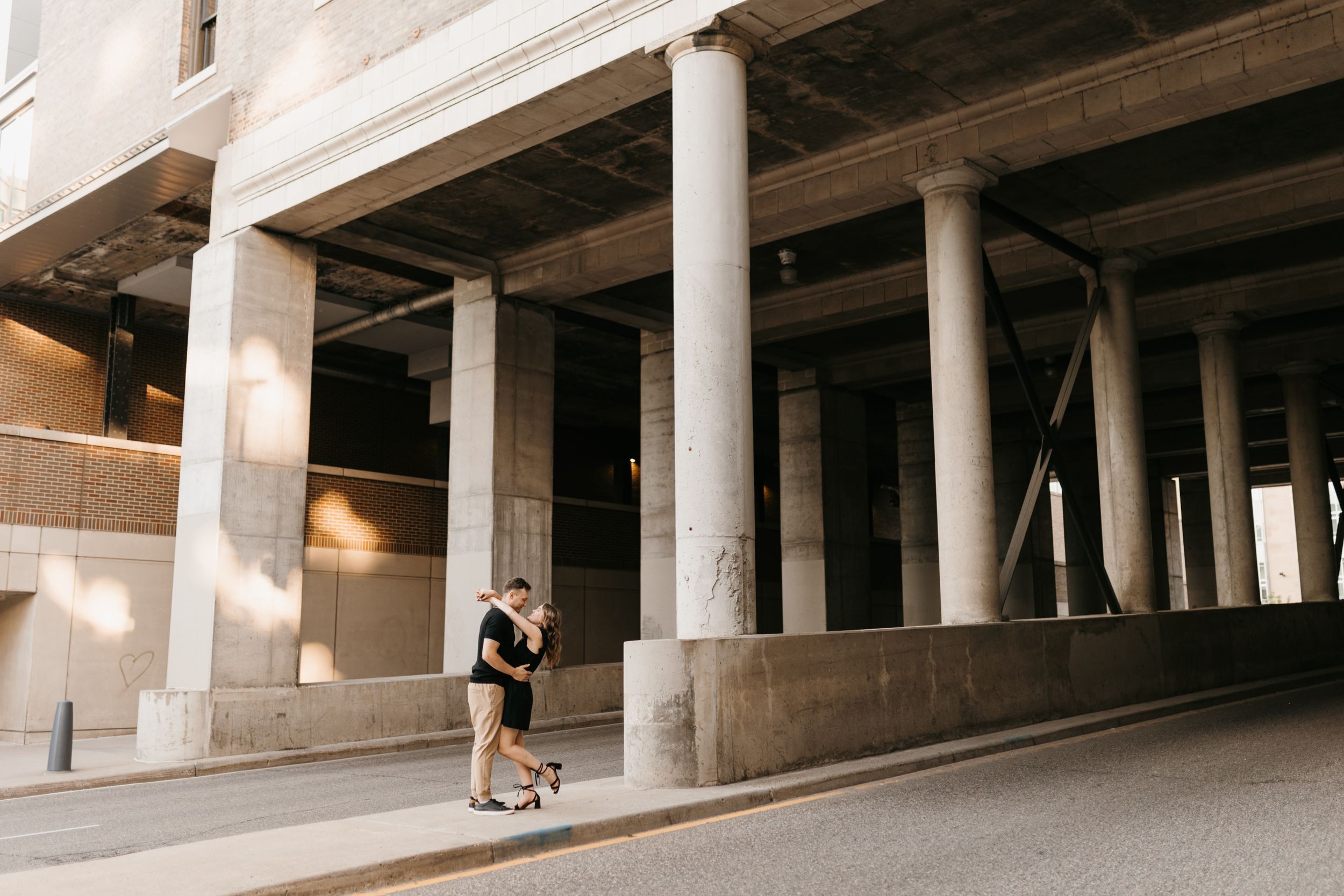 Couple sharing an intimate embrace under a large concrete structure with tall pillars in the city.