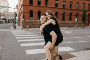 Smiling woman getting a piggyback ride from man in black shirt at an urban crosswalk.