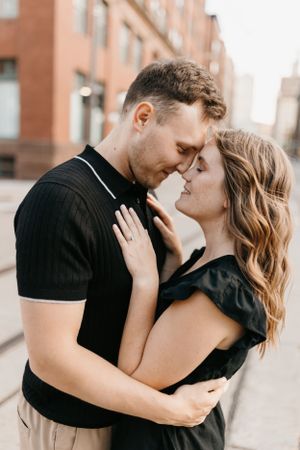 Couple sharing a tender nose-to-nose moment outdoors, woman in black dress with wavy hair.