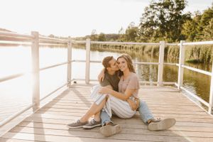 Happy couple sitting close together on a sunny wooden dock by a calm lake during golden hour.