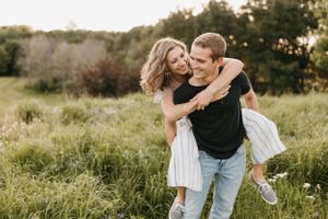 Joyful couple laughing as man gives woman a piggyback ride through a lush green meadow.