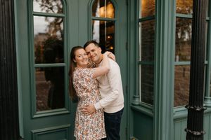 Couple embracing and smiling in front of green Victorian doors during fall engagement photos.