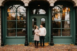Couple holding hands and smiling at each other before green ornate storefront windows in autumn.