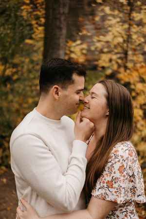 Romantic couple sharing a tender moment with a yellow leaf amid vibrant fall foliage backdrop.