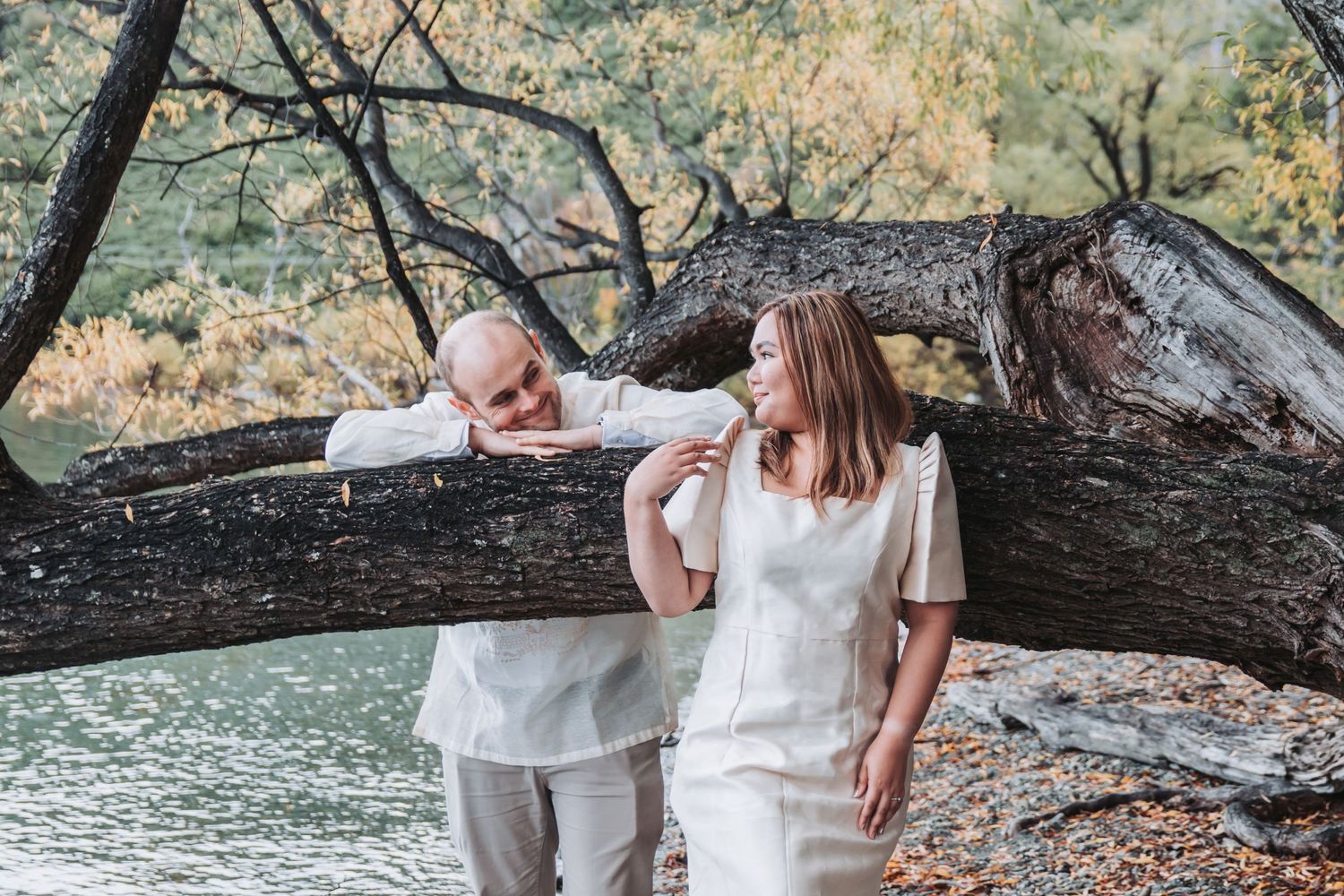 Two people share a joyful moment while leaning against a fallen tree trunk by the water.