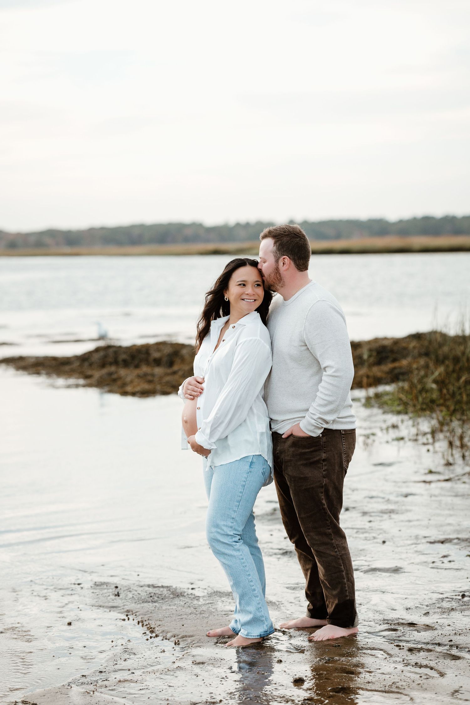 Couple embracing on a beach shoreline at dusk with water in the background.