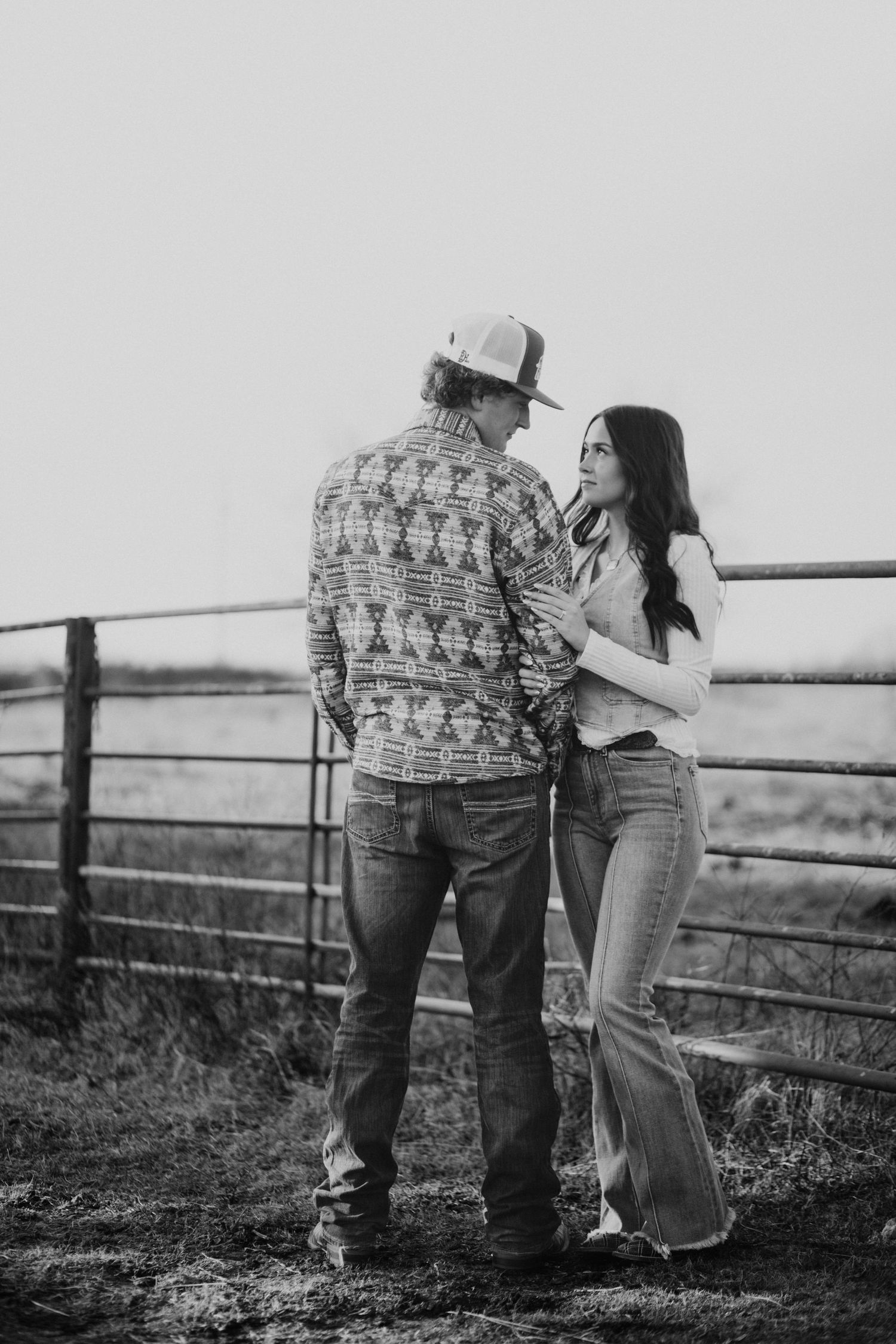 Black and white photo of couple sharing tender moment by rustic fence.