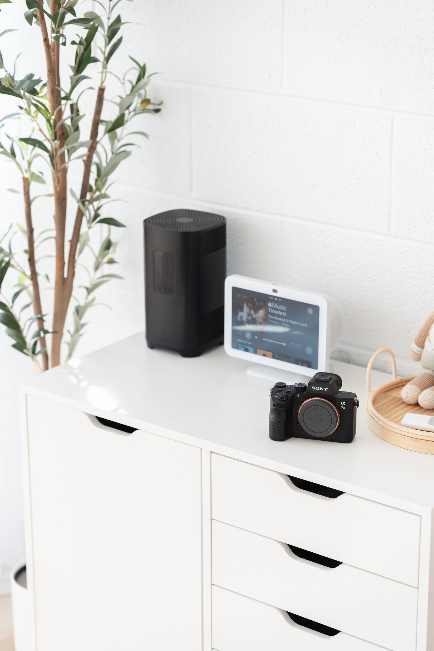 Modern white desk setup with camera equipment, plants and storage drawers.