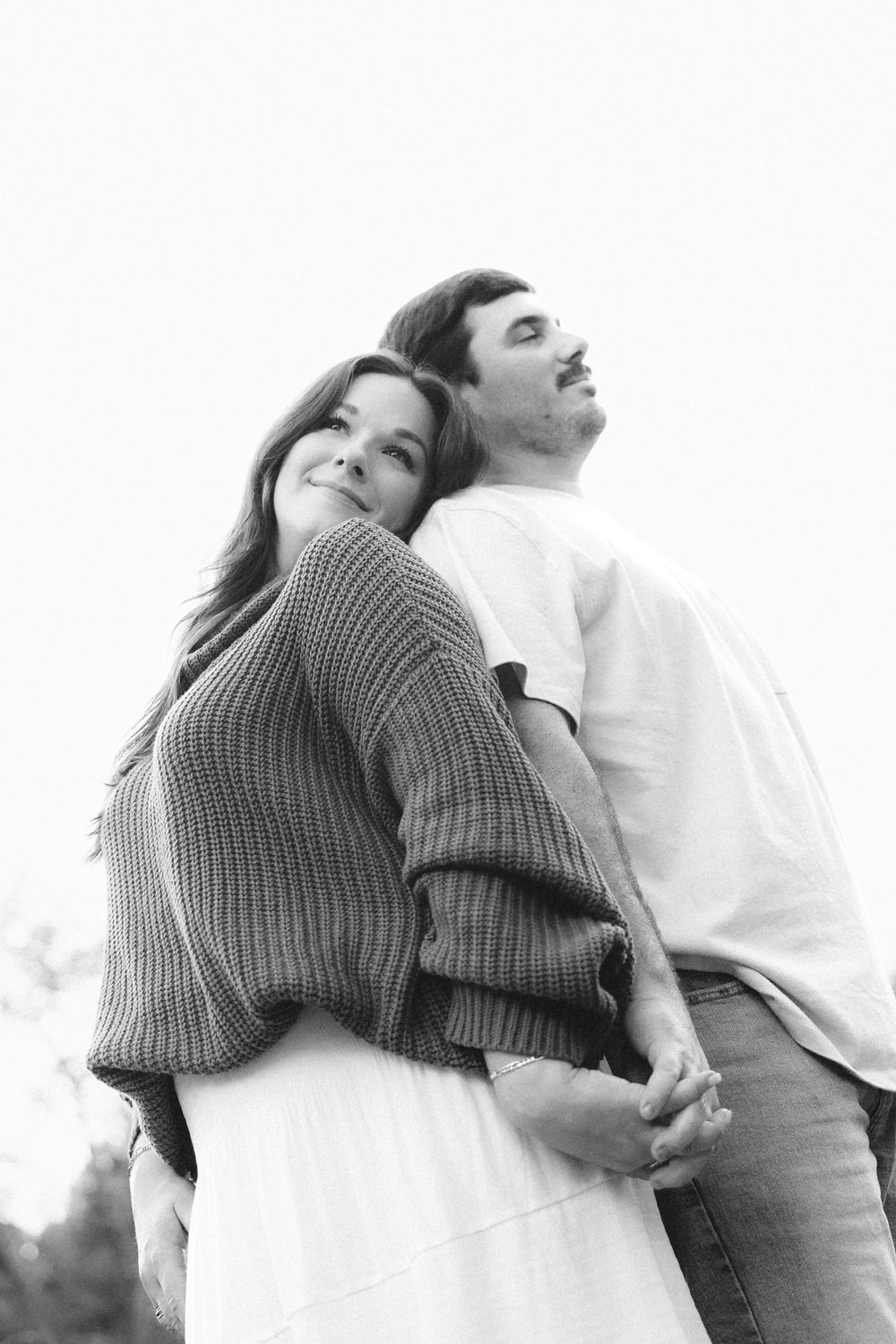 Black and white photo of a couple holding hands, woman smiling at camera while man looks away outdoors.