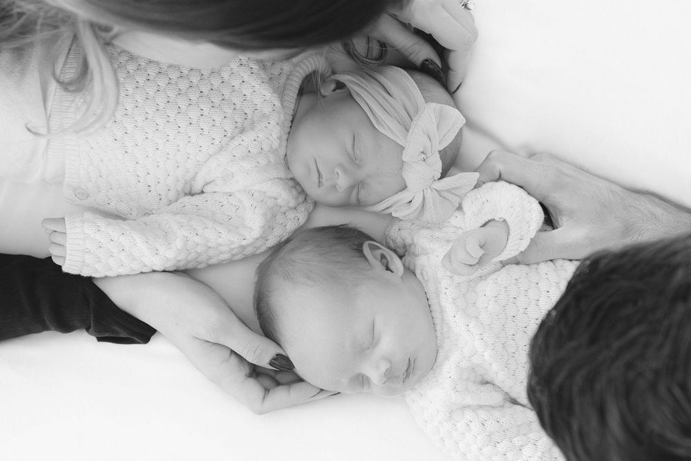 Two sleeping infants in white sweaters lying together on a soft white surface captured in black and white.