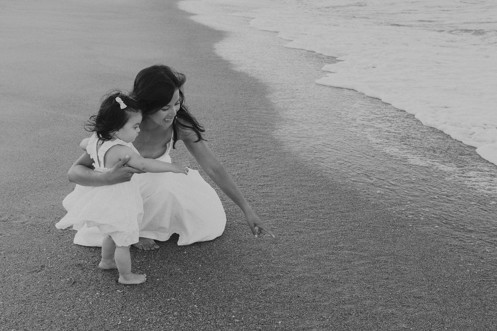 A sequence of artistic black and white photos showing a person in a white dress laying on a beach at sunset.