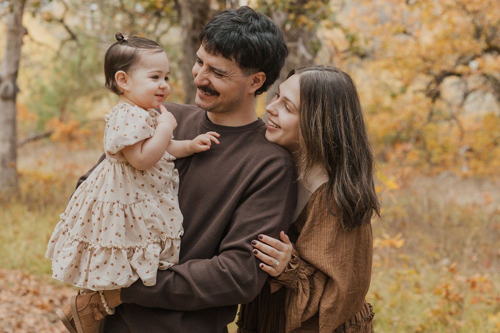 Family enjoying a tender moment together outdoors during autumn with golden foliage in background.