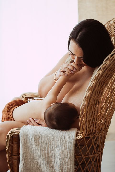 Tender moment of parent and infant bonding in soft natural light on wicker chair.