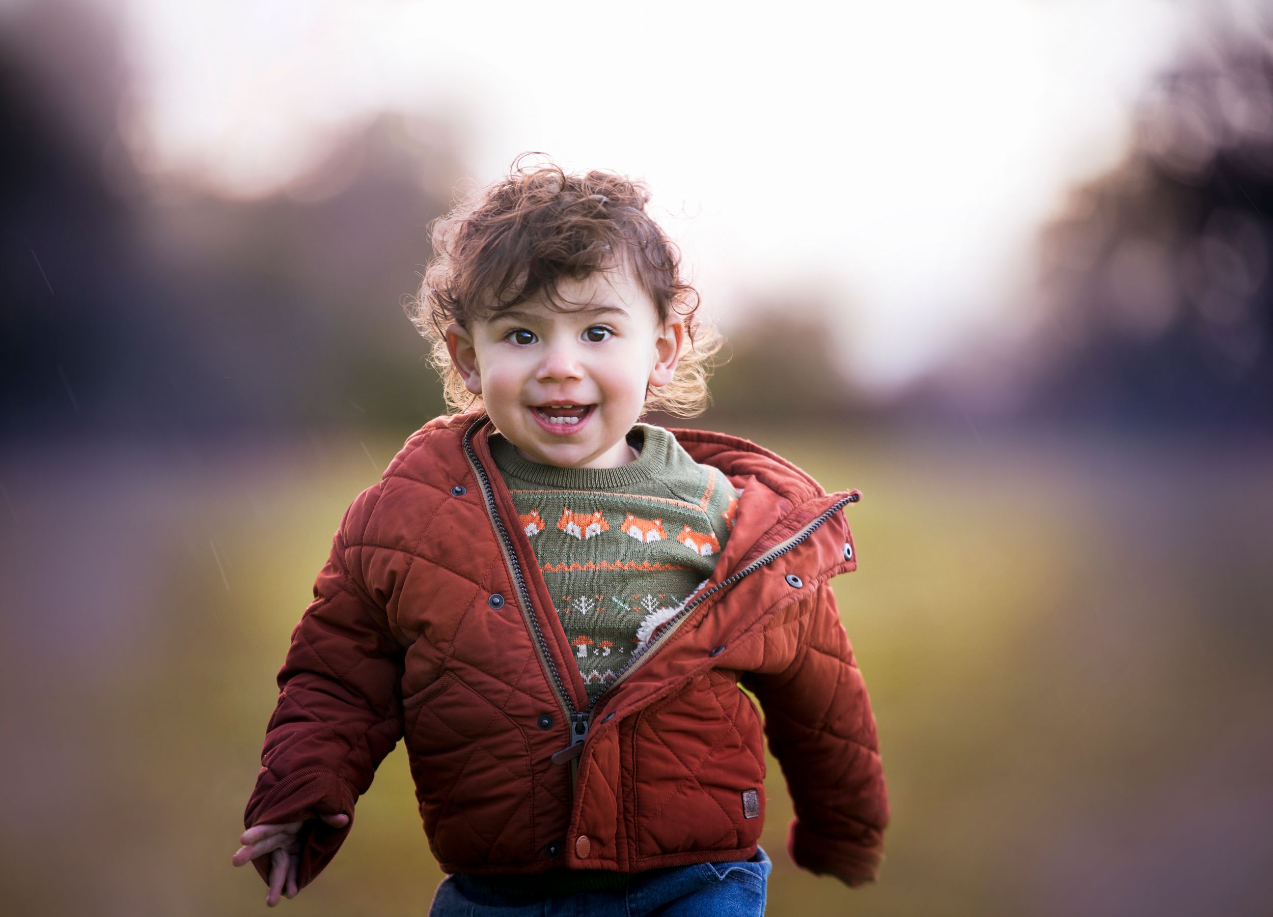 Child in a red winter coat and heart-patterned sweater smiling and playing outdoors in warm light.