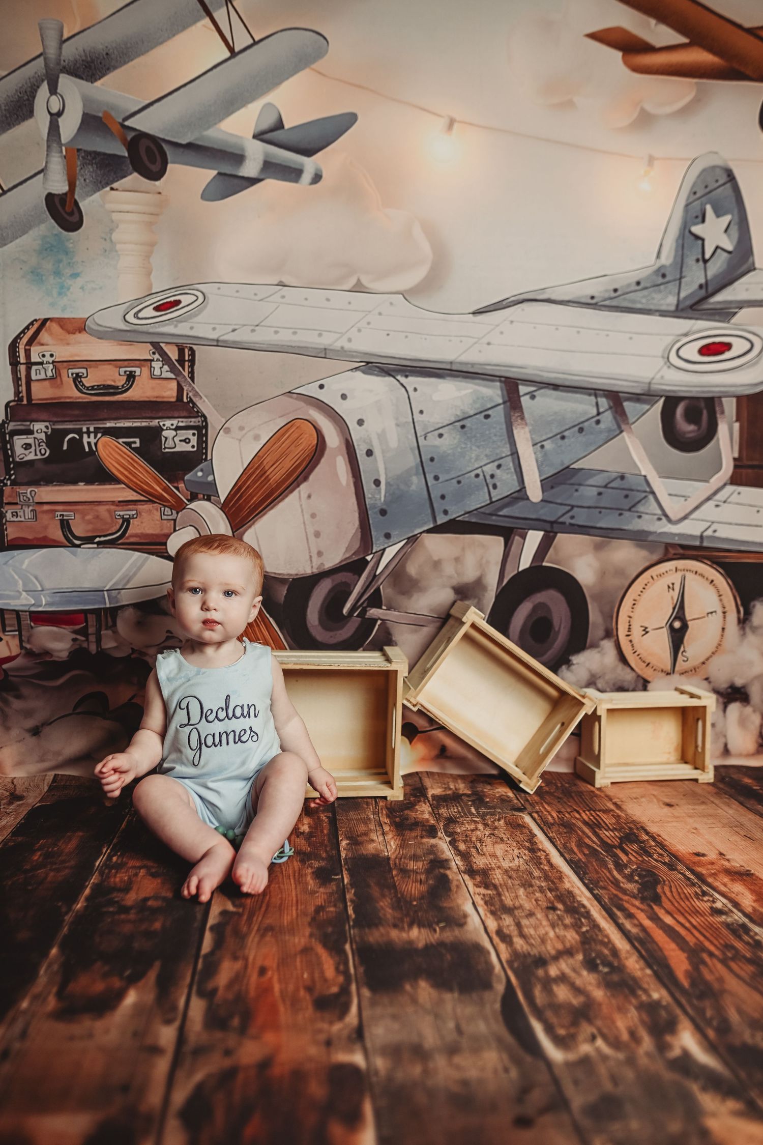 Vintage aviation themed newborn photo shoot with model planes, suitcases and rustic wooden backdrop.