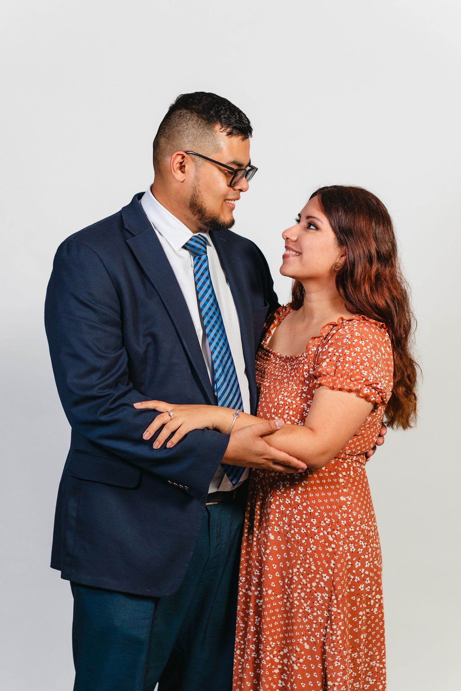 Couple embraces while wearing formal attire against white backdrop.