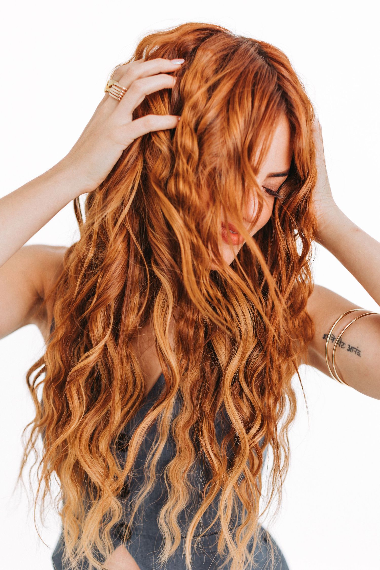 Close up of wavy copper-colored hair with hands running through it against white background.