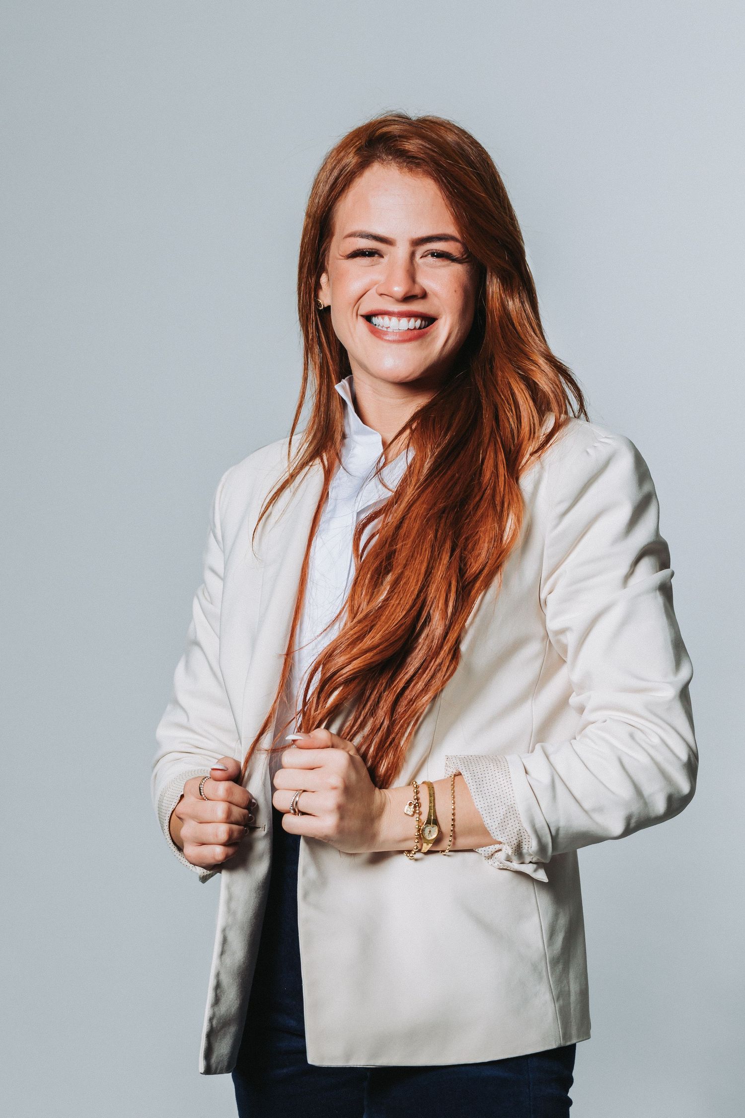 Professional portrait of woman with long red hair wearing white blazer and smiling.