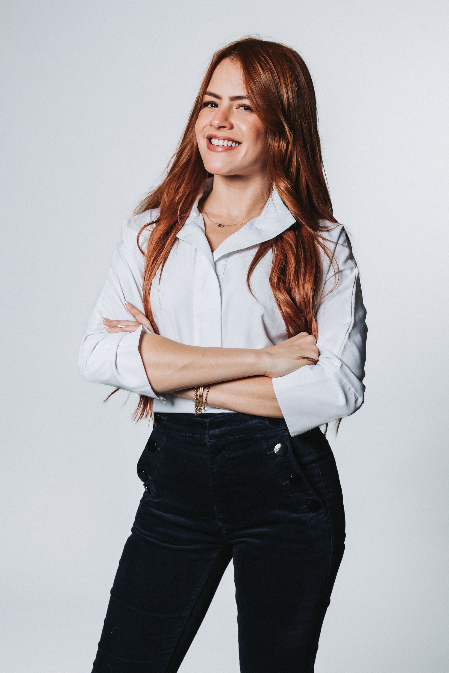 Business casual portrait of woman in white shirt and black pants with flowing red hair.