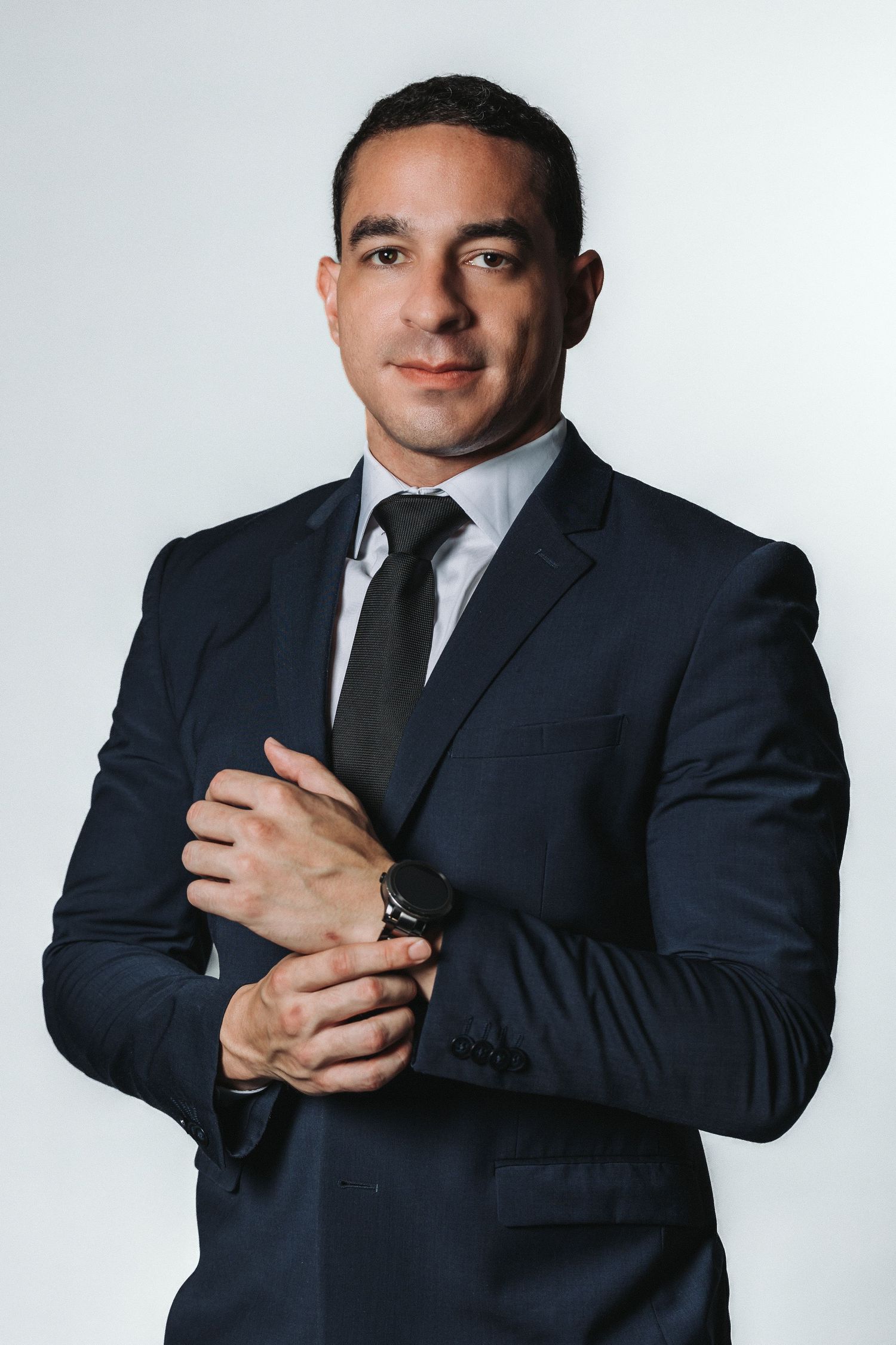 Professional headshot of man in dark suit and tie adjusting cufflinks against gray background.