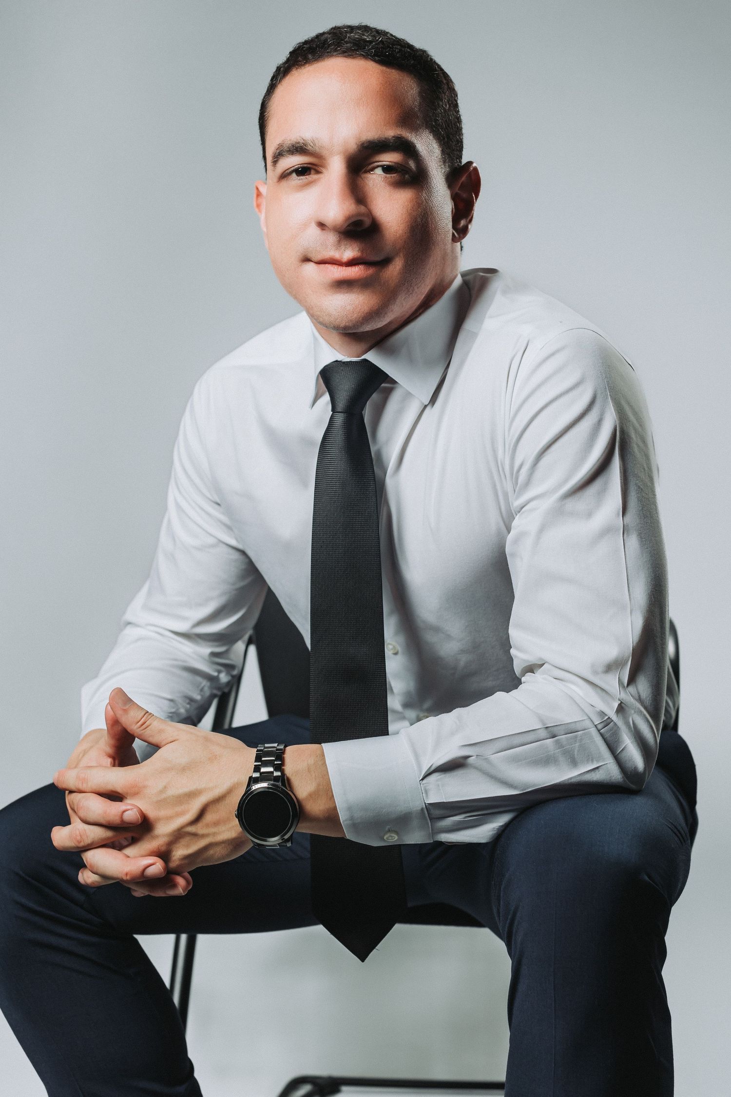 Professional headshot of a businessman in a white dress shirt and dark tie seated against a light background.