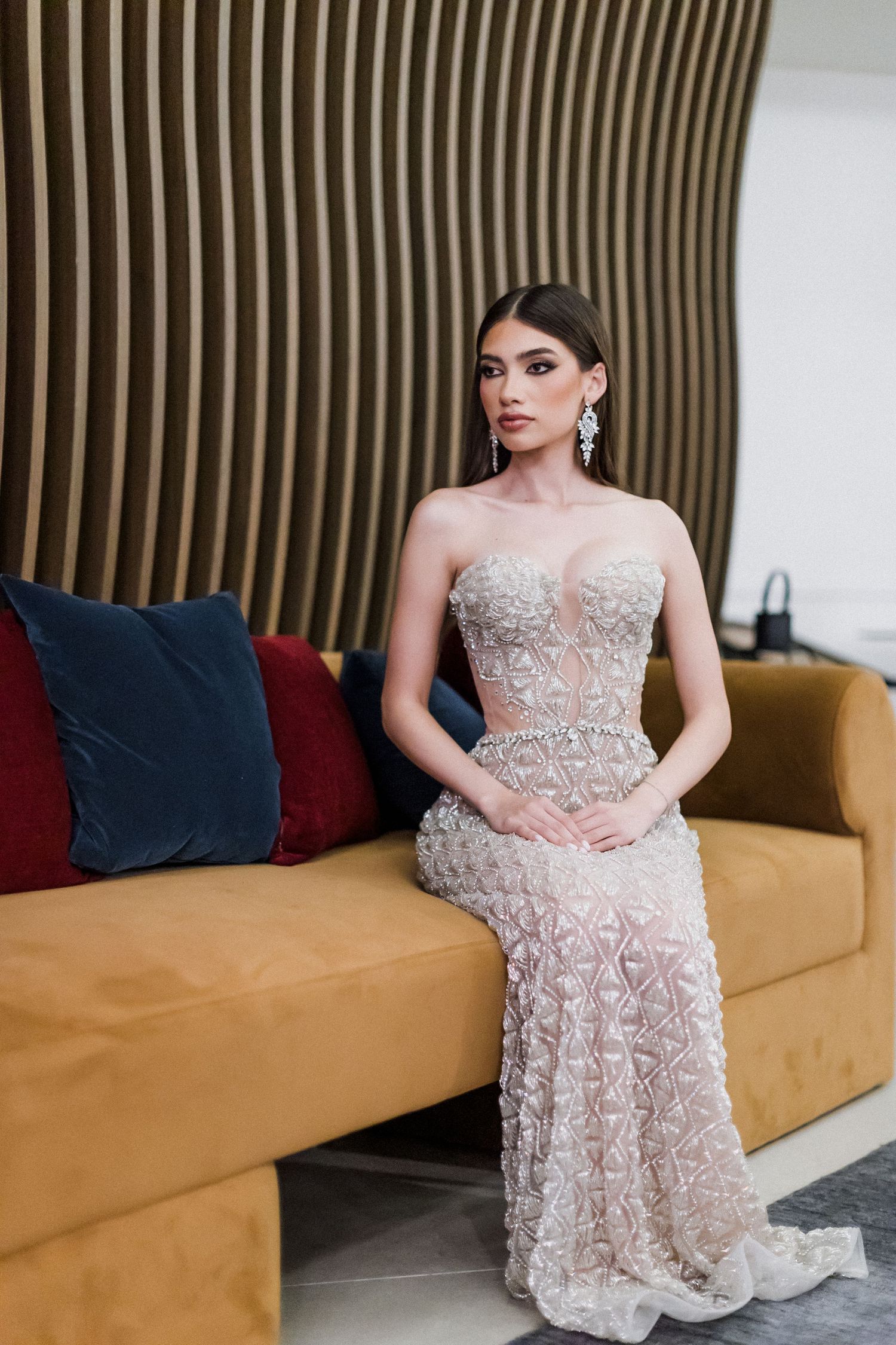 A formal sequence showing someone in a blush lace embellished gown posing elegantly on a tan modern sofa.