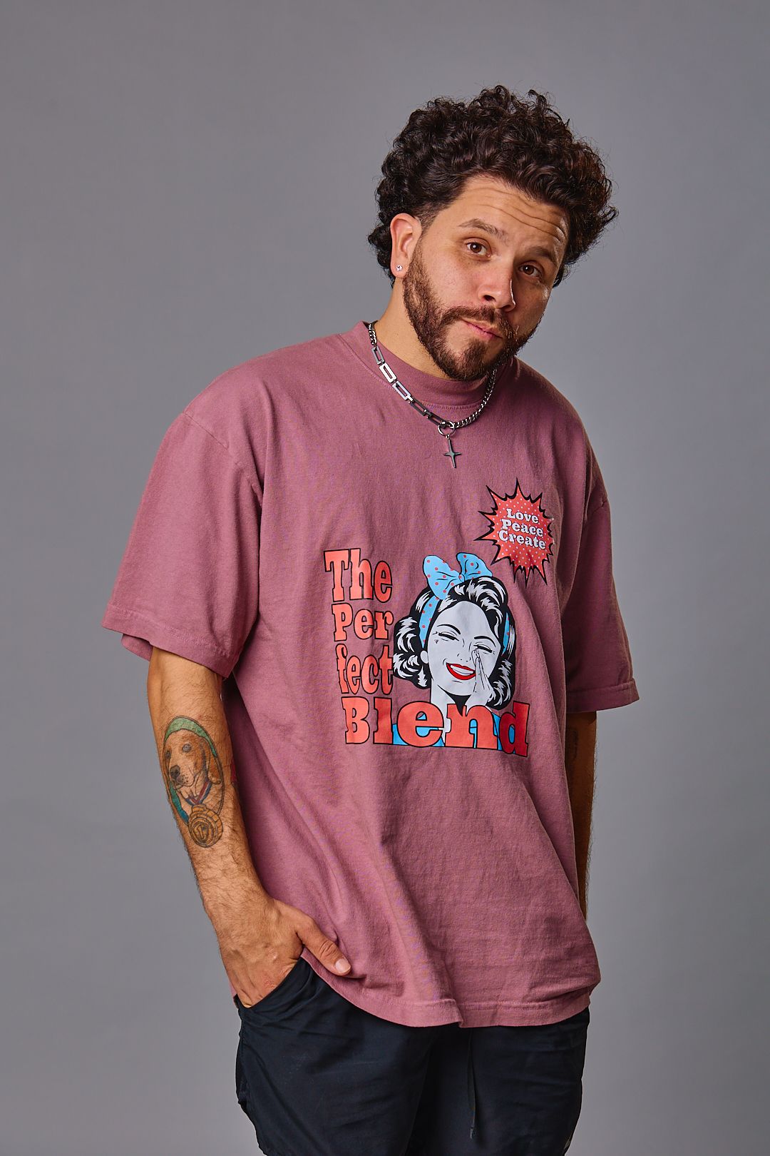 Person in pink graphic t-shirt with curly hair poses against grey background.