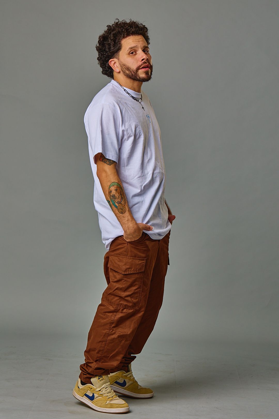 Casual style portrait of person in light shirt and brown cargo pants with yellow sneakers.