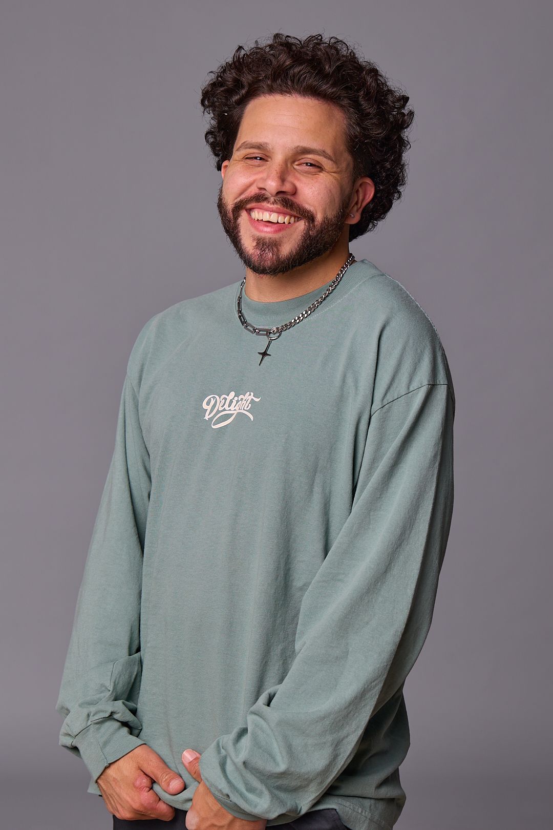 Portrait of person wearing mint green sweatshirt with necklace against grey backdrop.