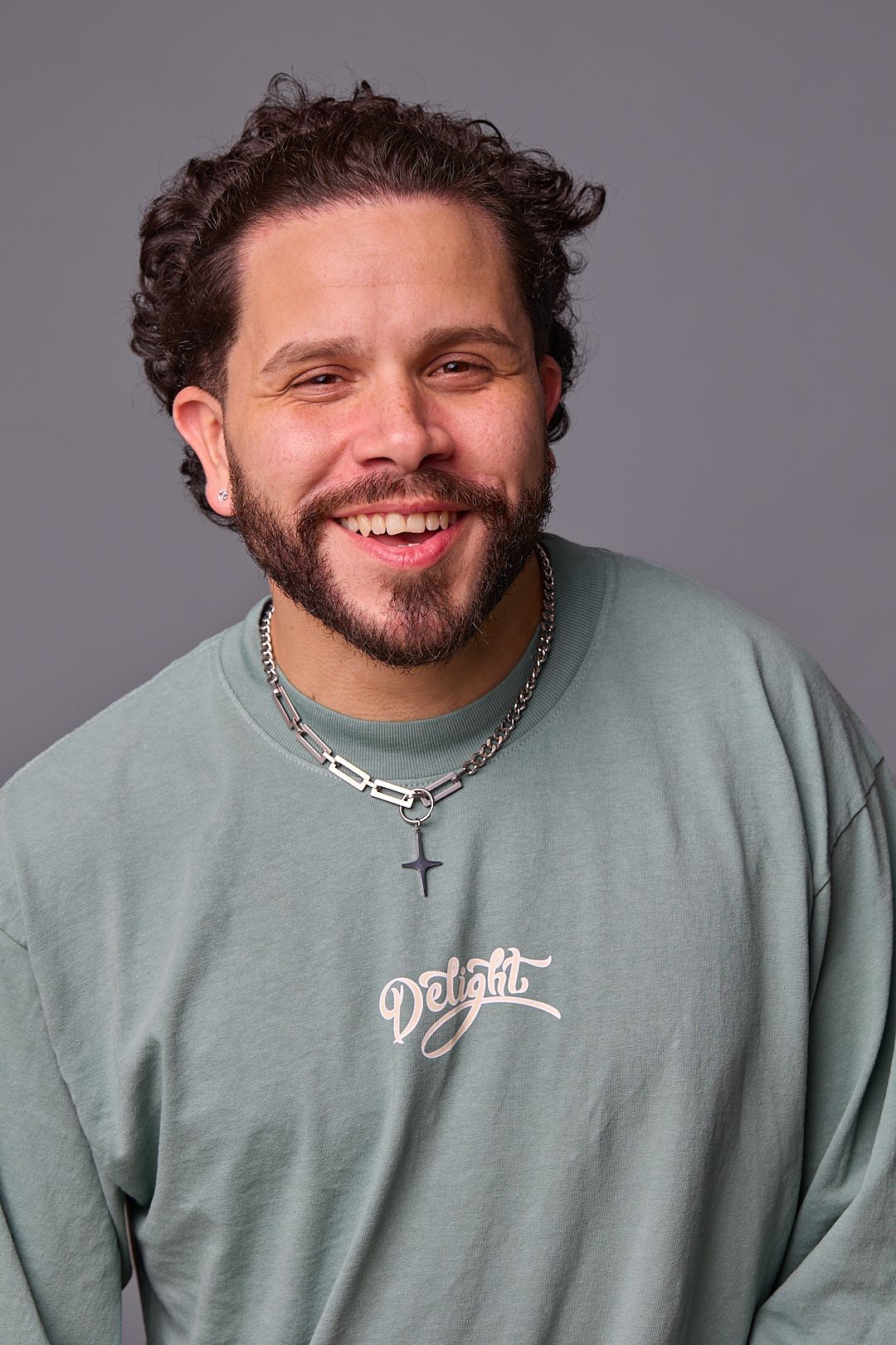Close-up portrait of person in mint sweatshirt with cross necklace against grey backdrop.