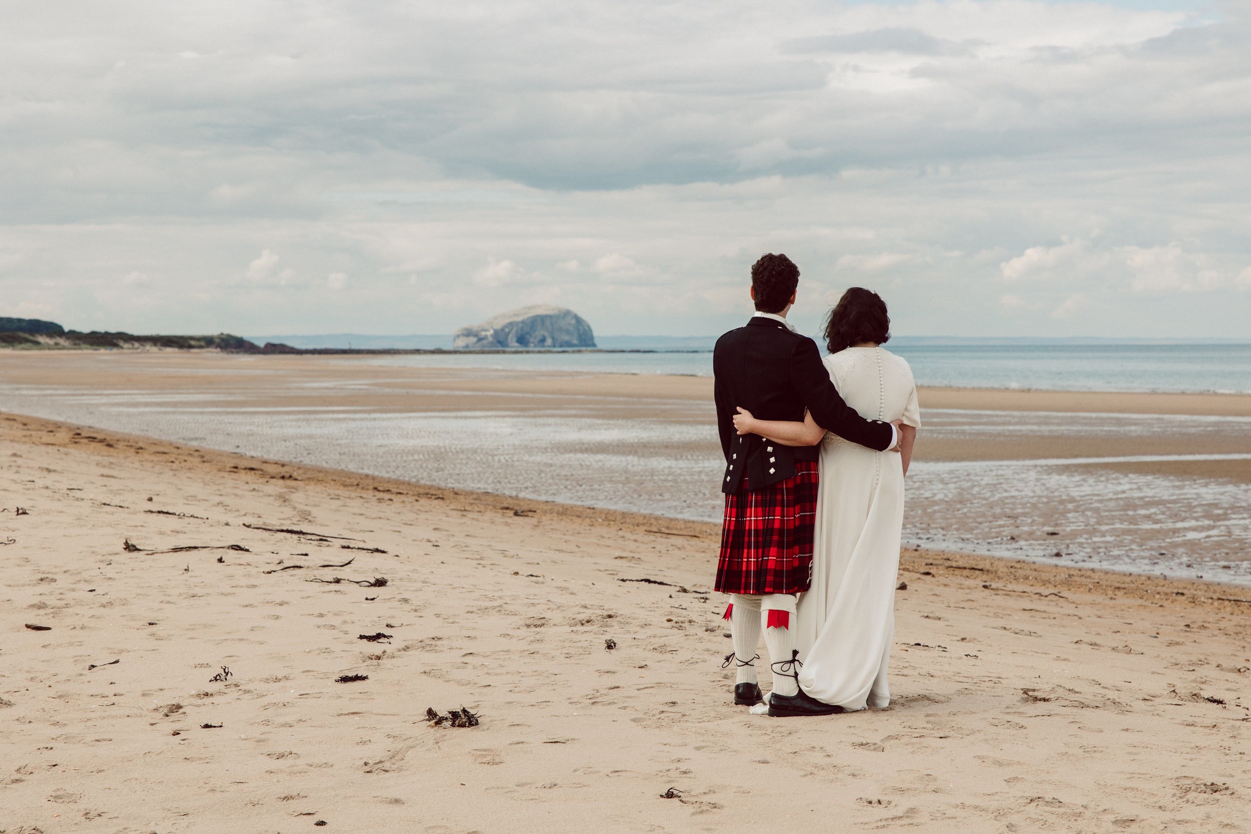 Couple sits together on a serene beach with cloudy skies.