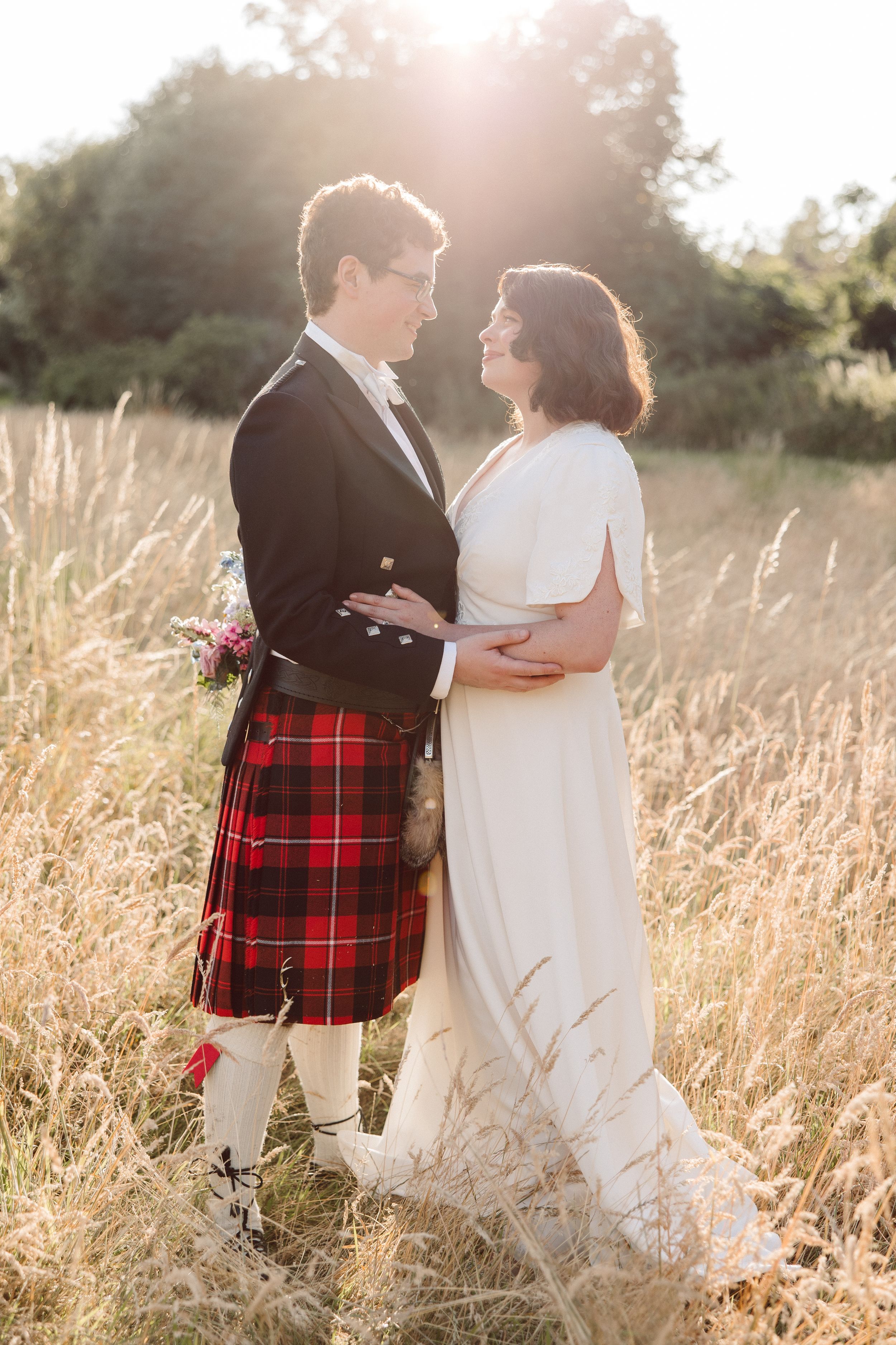 Couple poses intimately in golden sunlit field wearing formal attire.