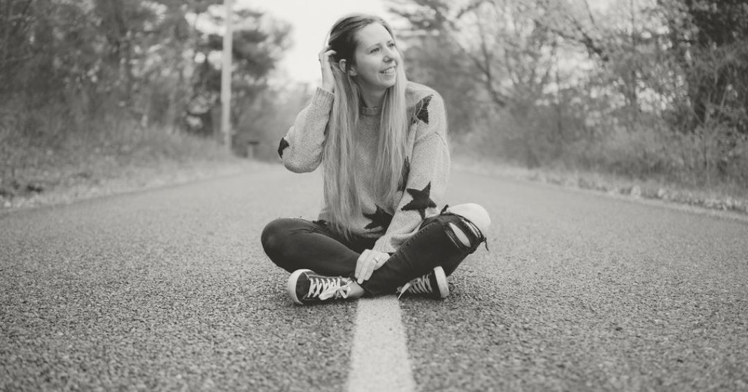 Person posing on empty autumn road with fall foliage in background.