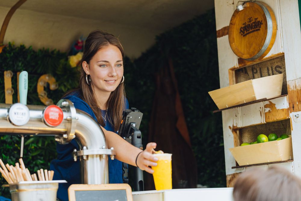 Server pouring fresh juice at outdoor beverage stand.