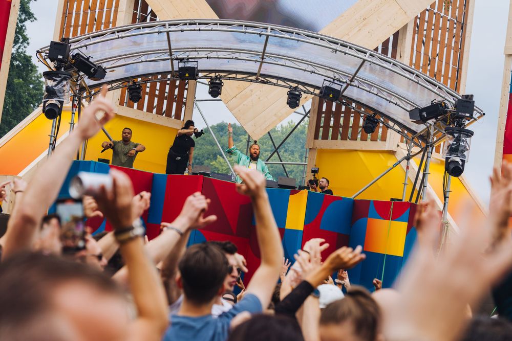 Energetic crowd with raised hands at outdoor concert with colorful stage setup.