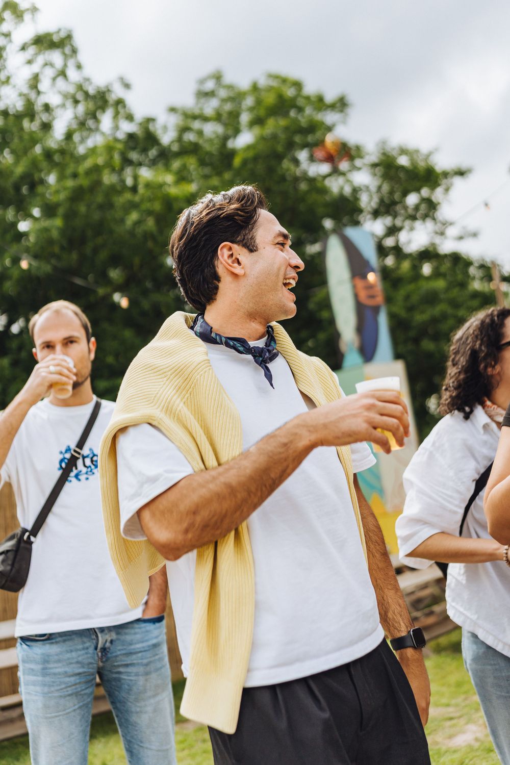Festival goer in yellow sweater enjoying drinks outdoors.