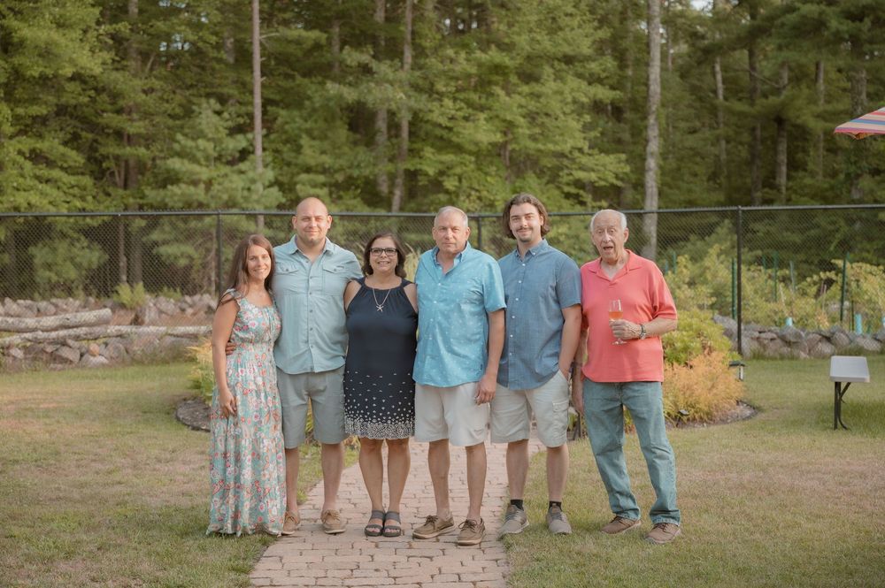 A group of people wearing coordinated blue and coral outfits pose together outdoors in a natural setting.