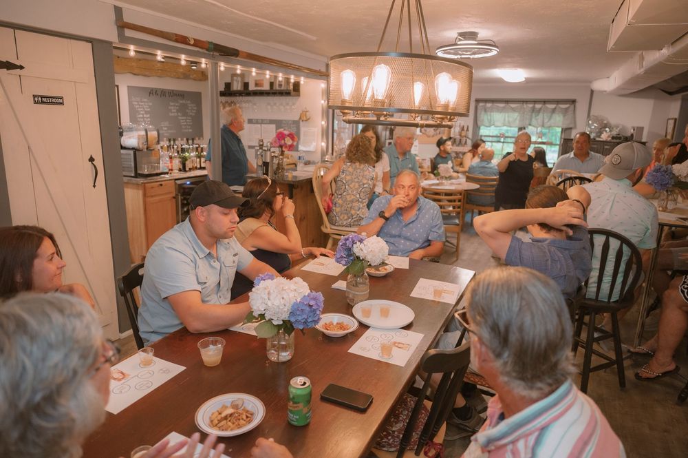 A group of people sit around a long wooden table in a restaurant dining room during a gathering.