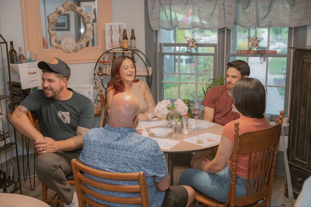 A group gathers around a small round table in a cozy dining area with natural light streaming through windows.