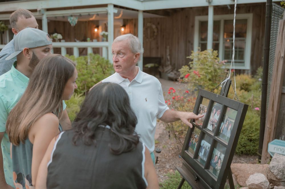 People gathered outdoors looking at framed photographs displayed near a porch.