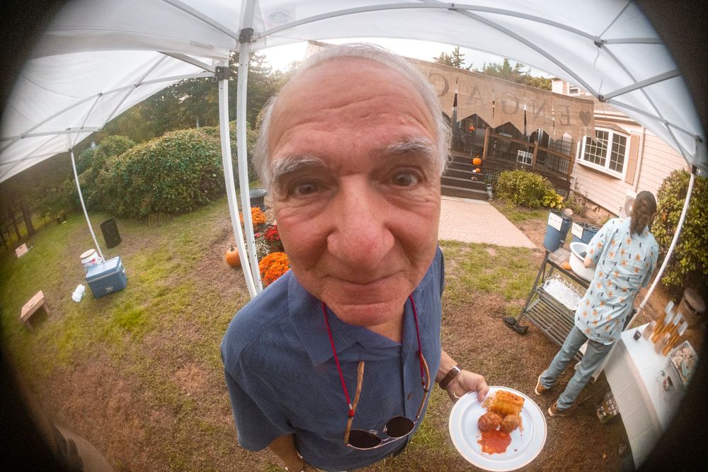 Close-up fisheye view of someone holding a small plate at an outdoor event.