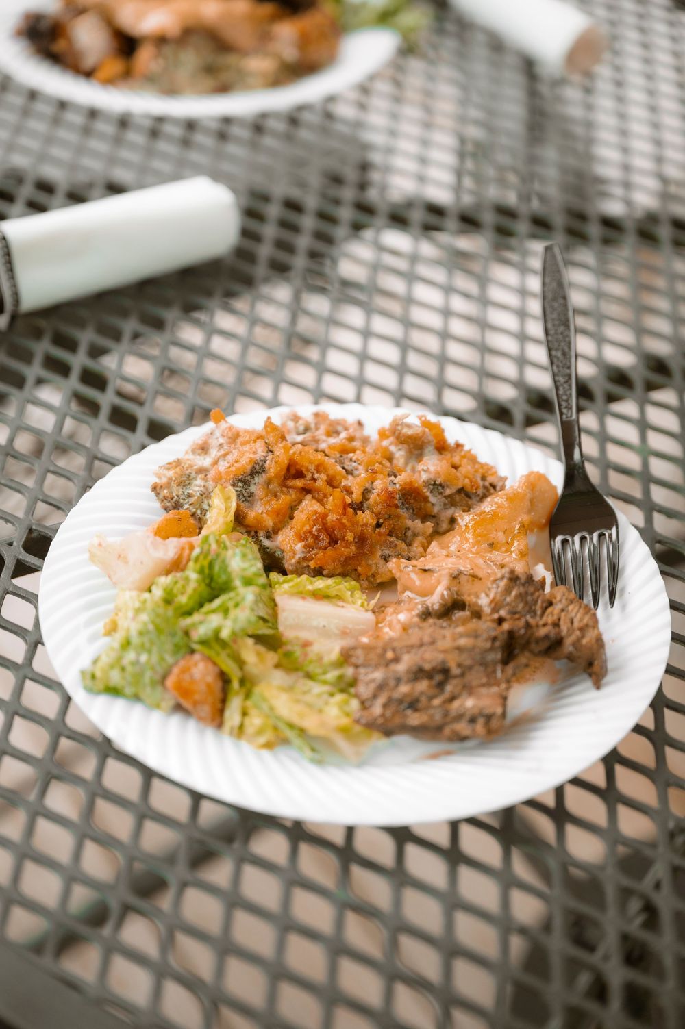 Multiple plates of fried chicken with side salad served on a metal mesh patio table outdoors.