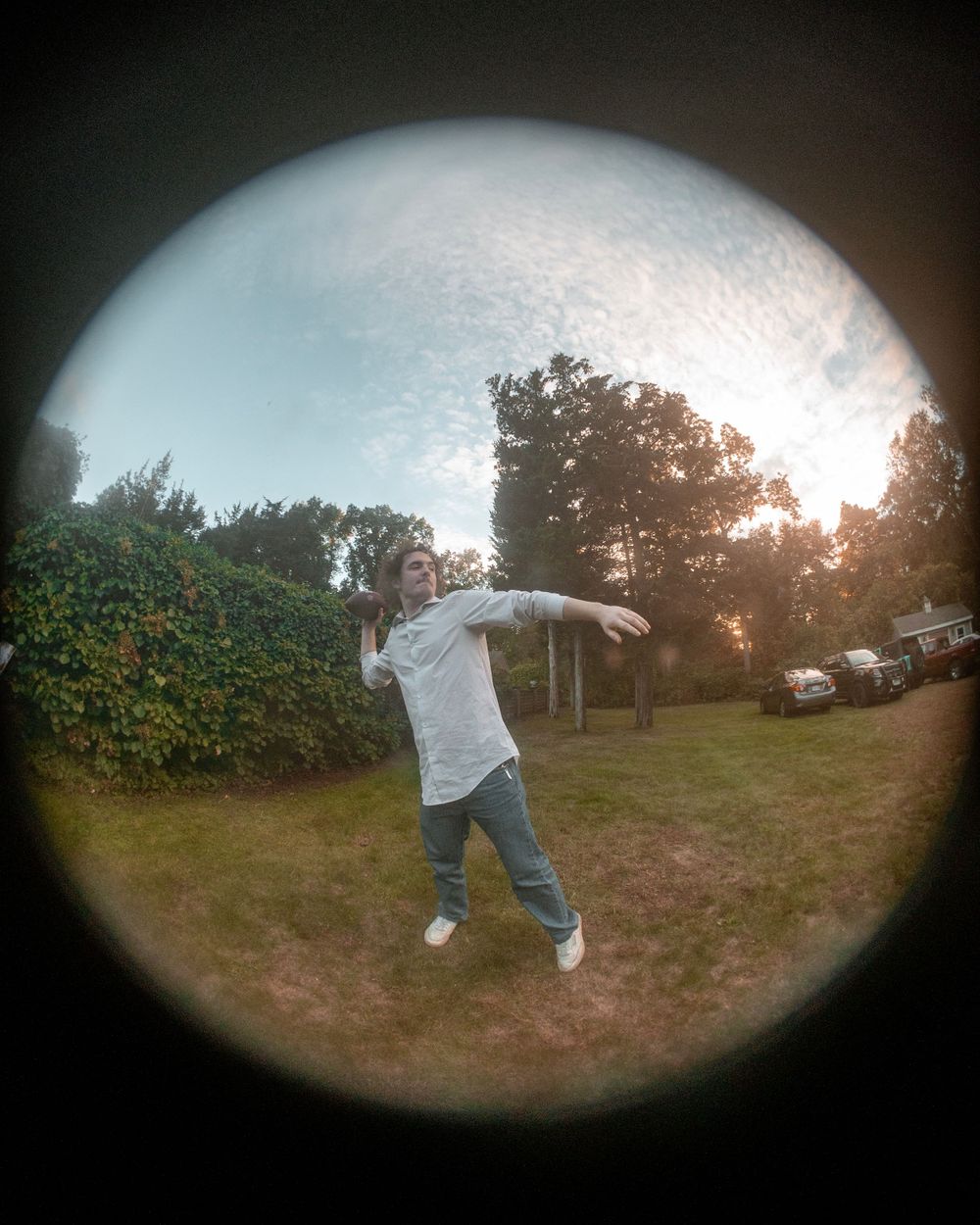 A fisheye lens photo captures someone posing outdoors at sunset against a garden backdrop.