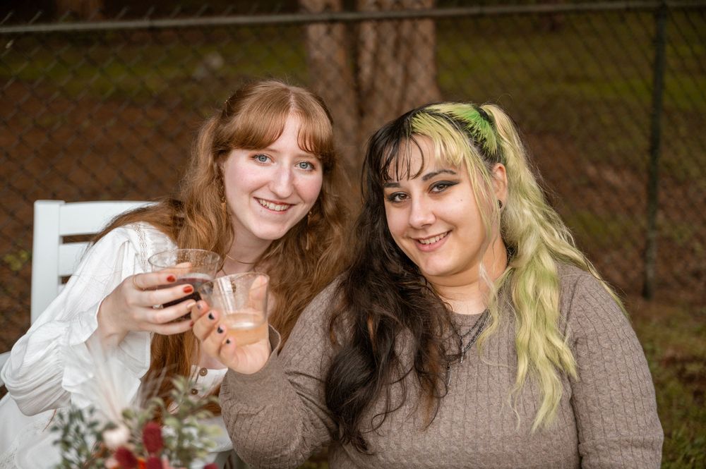Two young women share a warm moment together while holding drinks outdoors.